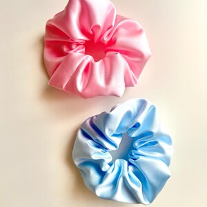 May include: Two satin scrunchies, one pink and one light blue. The scrunchies are made of soft, silky fabric and are perfect for holding hair in place.