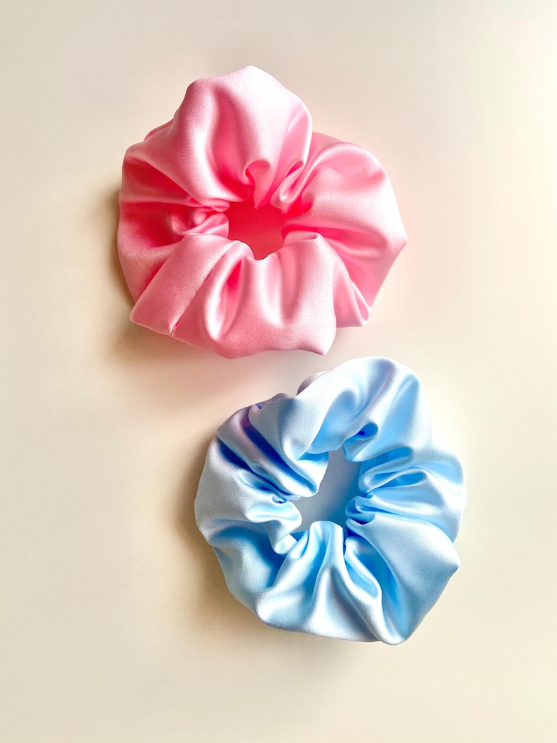 May include: Two satin scrunchies, one pink and one light blue. The scrunchies are made of soft, silky fabric and are perfect for holding hair in place.