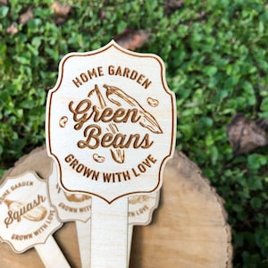 May include: Wooden garden markers with a rustic design. The markers feature the text "Home Garden Green Beans Grown With Love" and "Home Garden Squash Grown With Love".