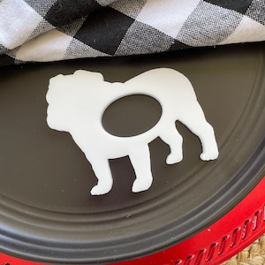 May include: White ceramic bulldog silhouette napkin ring on a black and red plate with a black and white checkered cloth napkin.