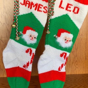 May include: Two red, white, and green knitted Christmas stockings with Santa Claus faces and the names "James" and "Leo" on them.
