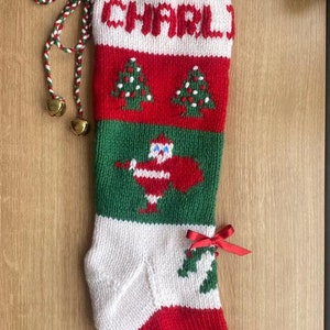 May include: A green, red, and white knitted Christmas stocking with the name "CHARLI" embroidered on the front. The stocking features a Santa Claus design and two Christmas trees.