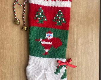 以下が含まれることがあります： 名前が「CHARLI」と刺繍された緑、赤、白のニット製のクリスマスストッキング。サンタクロースのデザインとクリスマスツリーが2本描かれています。