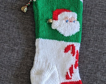 May include: A knitted Christmas stocking with a green, white, and red color scheme. The stocking has a Santa Claus face on the front, a candy cane design, and the name "MAX" embroidered on the top.