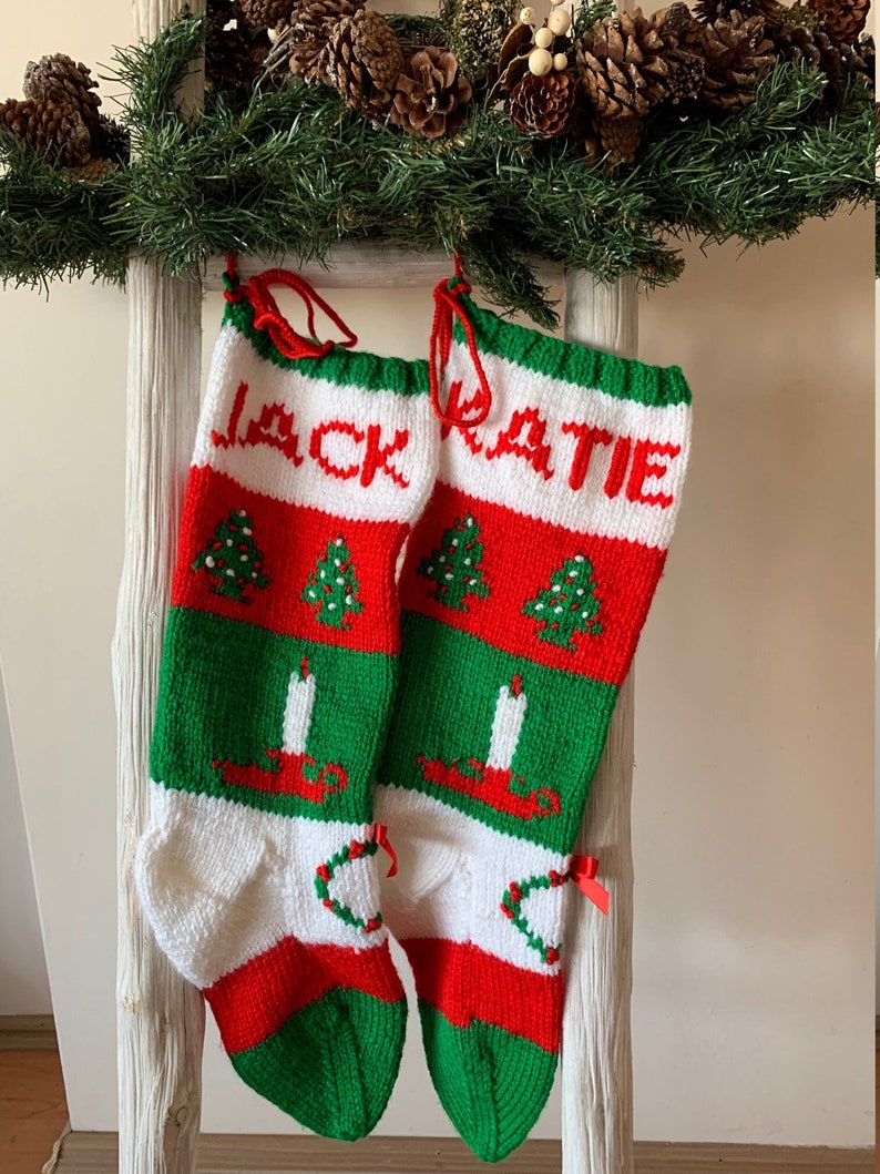 May include: Two red, white, and green knitted Christmas stockings with the names "Jack" and "Katie" embroidered on them. The stockings feature a pattern of Christmas trees, candles, and wreaths.