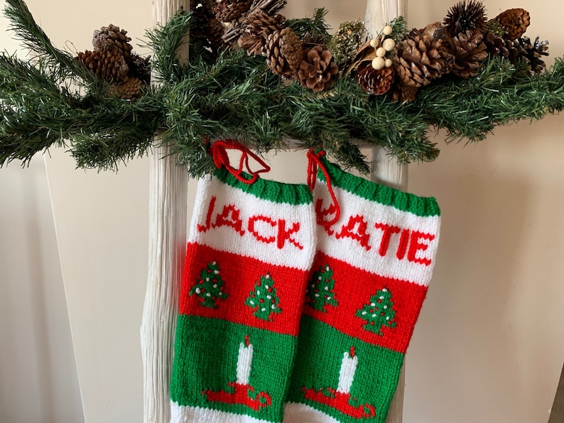 May include: Two red, white, and green knitted Christmas stockings with the names "Jack" and "Katie" embroidered on them. The stockings are decorated with small green Christmas trees and white candles.
