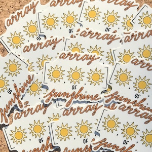 May include: A collection of white stickers with a yellow sun design and the words "array of sunshine" in a handwritten style. The stickers feature a bracketed design with three suns.