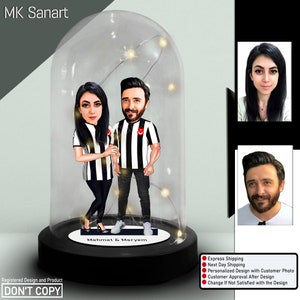 May include: A custom caricature of a couple in a glass dome with a light string inside. The couple is holding hands and wearing black and white striped shirts. The dome is on a black base with the text "Mehmet & Meryem".