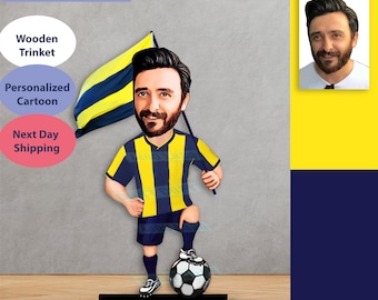 May include: A personalized cartoon figurine of a person holding a flag with yellow and black stripes. The figurine is wearing a blue and yellow striped jersey and black shorts. The figurine is standing on a black base with a white circle around it. The figurine is holding a soccer ball. The background is a gray wall with a yellow and blue wall on the right side.