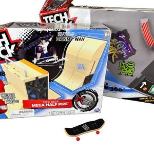May include: A Tech Deck Mega Half Pipe playset in a cardboard box featuring Danny Way branding, alongside a separate Tech Deck box and a small black fingerboard with red wheels. The packaging displays graphics of a half pipe and skate ramp.
