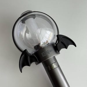 Puede incluir: Un bast&oacute;n de luz gris y negro con una parte superior transparente en forma de globo. El bast&oacute;n de luz tiene detalles de alas de murci&eacute;lago negras y las letras "EN-" impresas en la base. El mango tiene un bot&oacute;n plateado.