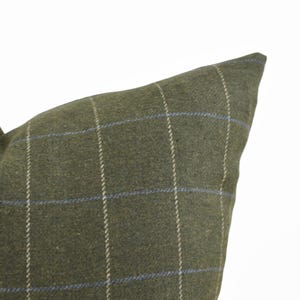 May include: A square throw pillow cover in a muted olive green fabric featuring a subtle windowpane check pattern. The design consists of thin, vertical and horizontal lines in light beige and soft blue, creating a grid across the surface.