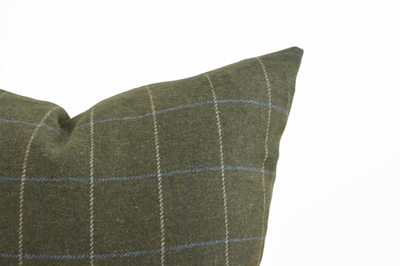 May include: A square throw pillow cover in a muted olive green fabric featuring a subtle windowpane check pattern. The design consists of thin, vertical and horizontal lines in light beige and soft blue, creating a grid across the surface.