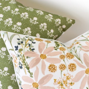 May include: Two decorative throw pillows. One pillow has a green background with a white floral pattern. The other pillow has a white background with large pink and yellow floral designs and green foliage.