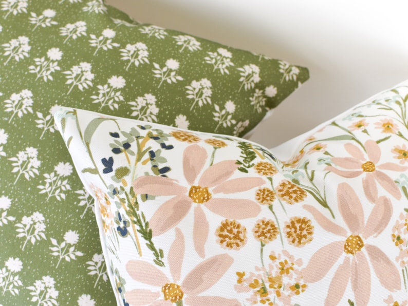 May include: Two decorative throw pillows. One pillow has a green background with a white floral pattern. The other pillow has a white background with large pink and yellow floral designs and green foliage.