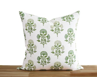 May include: A square throw pillow featuring a white fabric base with a repeating pattern of green floral motifs. The design consists of stylized green flowers with textured details and green leaves arranged in a symmetrical grid layout.