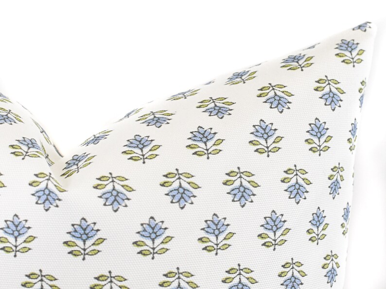 Puede incluir: Un coj&iacute;n blanco con un patr&oacute;n repetido de dise&ntilde;os florales azules y hojas verdes. El coj&iacute;n tiene un aspecto suave y texturizado, adecuado para la decoraci&oacute;n del hogar.
