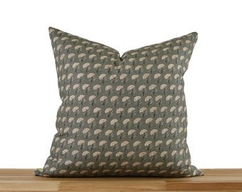 May include: Square decorative pillow with a repeating floral pattern in cream and dark gray on a muted green background. The pillow is placed on a wooden surface against a white backdrop. The pillow is a home decor item.