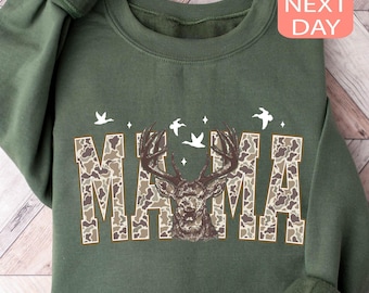 May include: Green sweatshirt with the word "MAMA" in camouflage print, featuring a deer head graphic and white bird silhouettes. The sweatshirt has a crew neck and long sleeves.