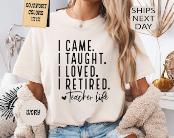 Op de afbeelding: Ivoor kleurig t-shirt met de tekst "I CAME. I TAUGHT. I LOVED. I RETIRED. Teacher life." Het shirt heeft ook een label met de tekst "Comfort Colors 1717". Het model draagt een spijkerbroekshort en een beige vest.