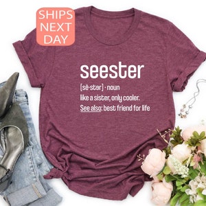 以下が含まれることがあります： 「seester」という言葉が「妹のような、ただもっとクールな」と定義された、マルーンのTシャツ。定義には「参照：生涯の親友」も含まれています。