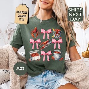K&ouml;nnte beinhalten: Gr&uuml;nes T-Shirt mit einem grafischen Aufdruck von Krebsen, rosa Schleifen und dem Text "COMFORT COLORS 1717".