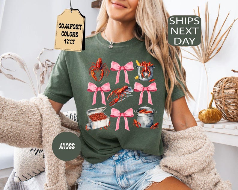 K&ouml;nnte beinhalten: Gr&uuml;nes T-Shirt mit einem grafischen Aufdruck von Krebsen, rosa Schleifen und dem Text "COMFORT COLORS 1717".