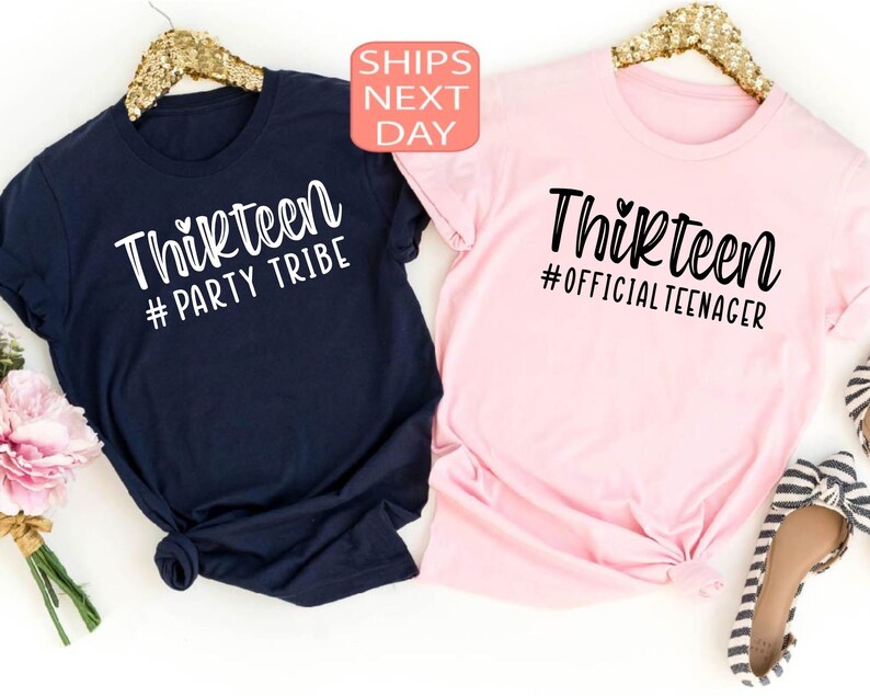 May include: Two t-shirts, one navy blue and one pink, with the text 'Thirteen' on them. The navy blue shirt has the text '#Party Tribe' and the pink shirt has the text '#Official Teenager'.