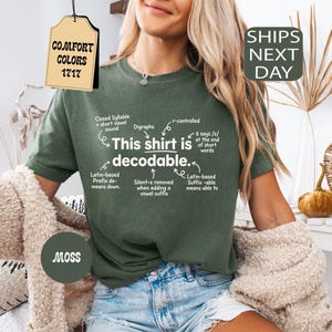 May include: A moss green short-sleeve t-shirt featuring white text that reads This shirt is decodable, surrounded by linguistic annotations including Closed Syllable, Digraphs, r-controlled, and Latin-based prefix and suffix explanations.