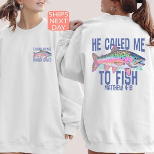 Peut inclure: Sweat-shirt blanc avec un motif de poisson color&eacute; au dos et un motif de poisson plus petit sur le devant. Le motif dorsal comprend le texte "HE CALLED ME TO FISH" et "MATTHEW 4:19". Le motif avant dit "FISHING LICENSE HEAVEN ISSUED".