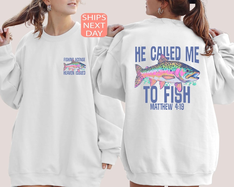 Peut inclure: Sweat-shirt blanc avec un motif de poisson color&eacute; au dos et un motif de poisson plus petit sur le devant. Le motif dorsal comprend le texte "HE CALLED ME TO FISH" et "MATTHEW 4:19". Le motif avant dit "FISHING LICENSE HEAVEN ISSUED".