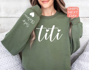 May include: Green sweatshirt with the text "titi" in white cursive lettering with three small white hearts above the text. The left sleeve has the text "Godly Grown" in white cursive lettering with a small white heart.