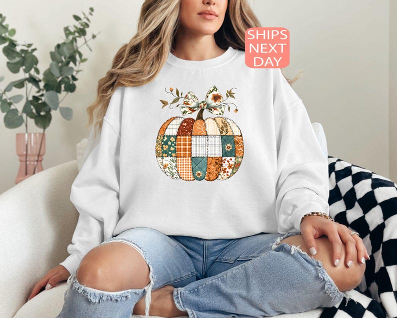 May include: White sweatshirt featuring a patchwork pumpkin design with floral and plaid patterns in orange, green, and brown. The pumpkin has a floral bow on top. The text "SHIPS NEXT DAY" is in a pink box.