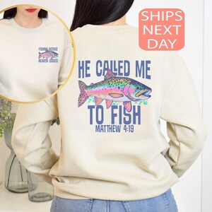 Peut inclure: Sweat-shirt cr&egrave;me avec un motif de poisson color&eacute; et le texte "He Called Me To Fish" et "Matthew 4:19". Un petit motif sur le devant indique "Fishing License Heaven Issued".