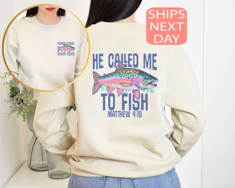 Peut inclure: Sweat-shirt cr&egrave;me avec un motif de poisson color&eacute; et le texte "He Called Me To Fish" et "Matthew 4:19". Un petit motif sur le devant indique "Fishing License Heaven Issued".