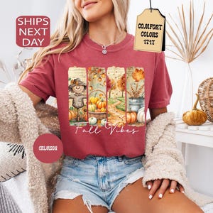 May include: Crimson-colored t-shirt with a fall-themed graphic. The graphic features a scarecrow, pumpkins, and the text "Fall Vibes." The shirt is a Comfort Colors 1717 style.