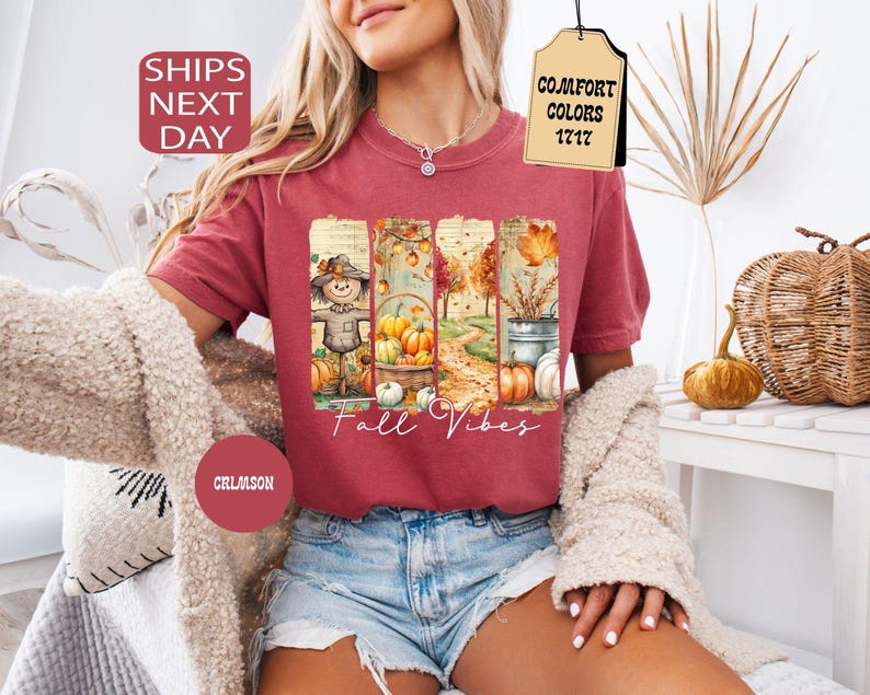 May include: Crimson-colored t-shirt with a fall-themed graphic. The graphic features a scarecrow, pumpkins, and the text "Fall Vibes." The shirt is a Comfort Colors 1717 style.