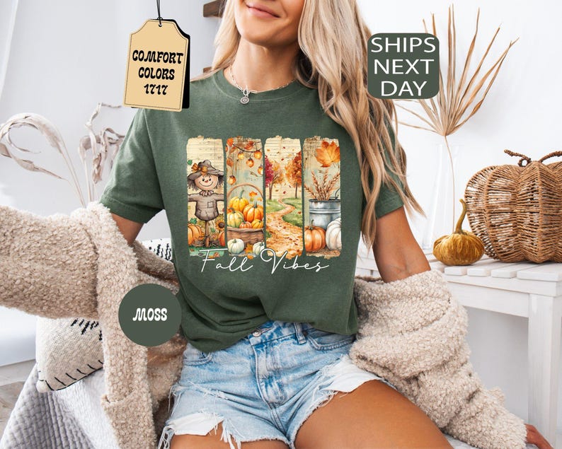 May include: Moss green t-shirt with a fall-themed graphic. The graphic features a scarecrow, pumpkins, and autumn foliage. The words "Fall Vibes" are written in a script font. The shirt is part of the Comfort Colors 1717 collection.