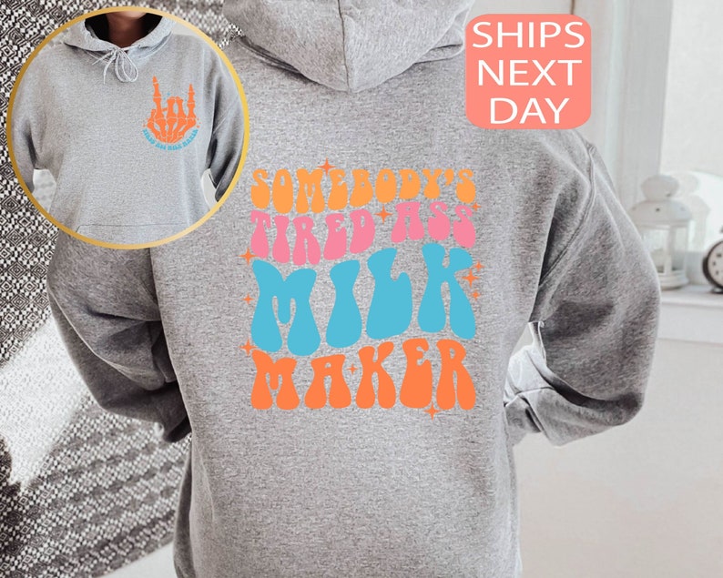 May include: A gray hoodie with the text "SOMEBODY'S TIRED ASS MILK MAKER" in colorful retro font on the back. The front left chest features a skeleton hand graphic with the text "GOOD DAY MILK MAKER".