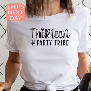 May include: White t-shirt with the text "Thirteen #Party Tribe" in black lettering. A small heart symbol is above the word "Thirteen".