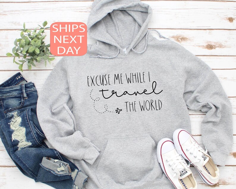 Może przedstawiać: Szara bluza z kapturem z napisem "Przepraszam, podczas gdy podr&oacute;żuję po świecie" i małym rysunkiem samolotu.