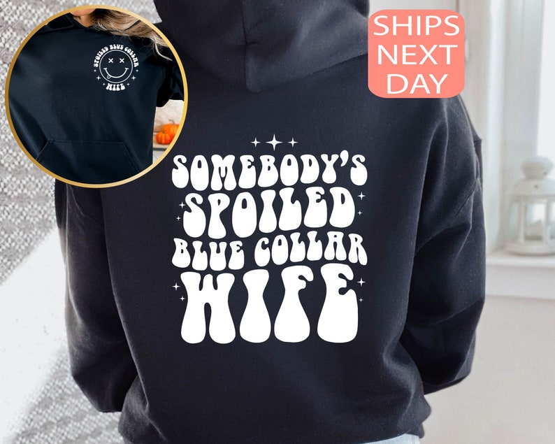 以下が含まれることがあります： 白い文字で「Somebody's Spoiled Blue Collar Wife」と書いてある黒いフード付きスウェットシャツ。レトロなフォントで書かれており、星で囲まれています。
