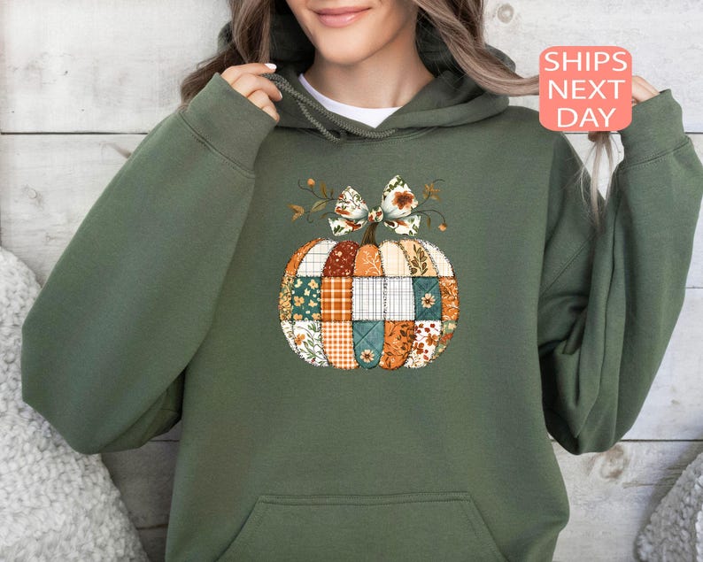 May include: Green hoodie featuring a patchwork pumpkin design with a floral bow. The pumpkin is composed of various fabric patterns in orange, white, and teal. The hoodie has a front pocket and a drawstring hood.