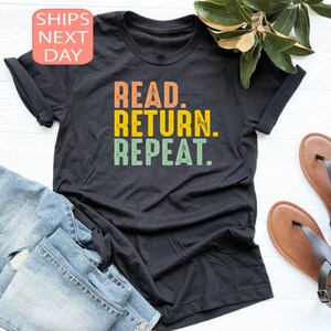 以下が含まれることがあります： オレンジ、黄色、緑で「READ. RETURN. REPEAT.」と書かれた黒いTシャツ。シャツはブルージーンズと茶色のサンダルと組み合わせています。テキストは、ヴィンテージスタイルです。