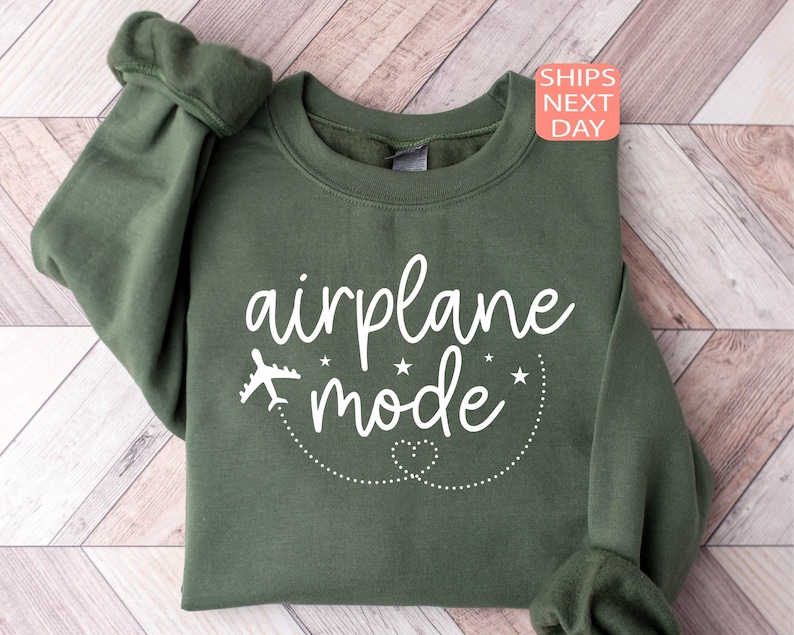 K&ouml;nnte beinhalten: Ein gr&uuml;ner Pullover mit dem Text "airplane mode" in wei&szlig;en Buchstaben. Oberhalb des Textes befindet sich ein kleines Flugzeugsymbol, unterhalb des Textes eine gepunktete Linie mit einem Herz.
