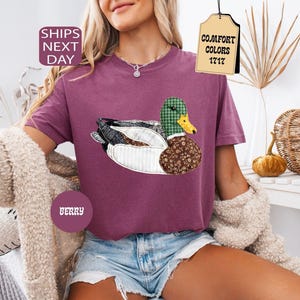 May include: Berry-colored t-shirt featuring a duck applique with plaid, floral, and white fabric details. The duck has a green plaid head and a yellow beak. The shirt has a relaxed fit and is paired with denim shorts.
