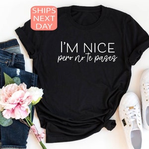 May include: Black t-shirt with the white text "I'M NICE pero no te pases". The shirt is styled with blue jeans, white sneakers, and a bouquet of pink and white flowers. A pink and white "SHIPS NEXT DAY" sticker is in the top left corner.
