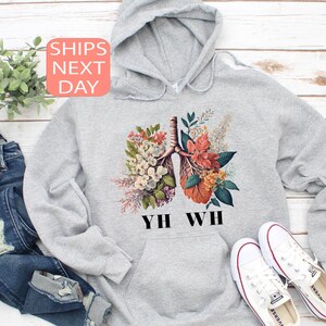 May include: Gray hoodie with a floral illustration of lungs and the text "YHW WH" printed on the front.