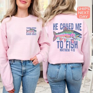Peut inclure: Sweat-shirt rose clair avec un motif de poisson color&eacute; et le texte "FISHING LICENSE HEAVEN ISSUED" sur le devant. Le dos pr&eacute;sente un motif de poisson plus grand et le texte "HE CALLED ME TO FISH MATTHEW 4:19".