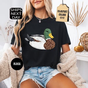 May include: Black t-shirt featuring a patchwork duck design with green, brown, and white patterns. The shirt has the text "Comfort Colors 1717" on a tag and "Ships Next Day" on a black circle.